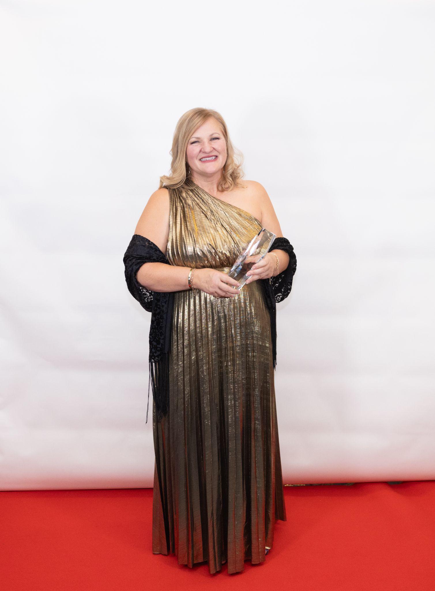 Woman in gold dress holding an award, standing on a red carpet