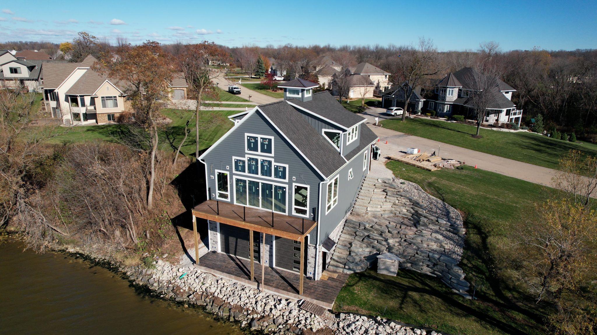 A modern gray house by the water with a stone patio and surrounding trees