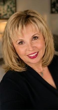 Smiling woman with blonde hair and red lipstick in a soft indoor setting