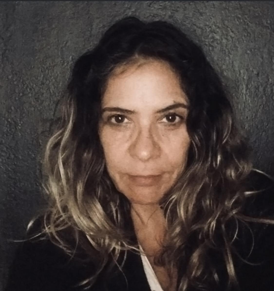 A woman with curly hair poses for a close-up selfie against a dark background