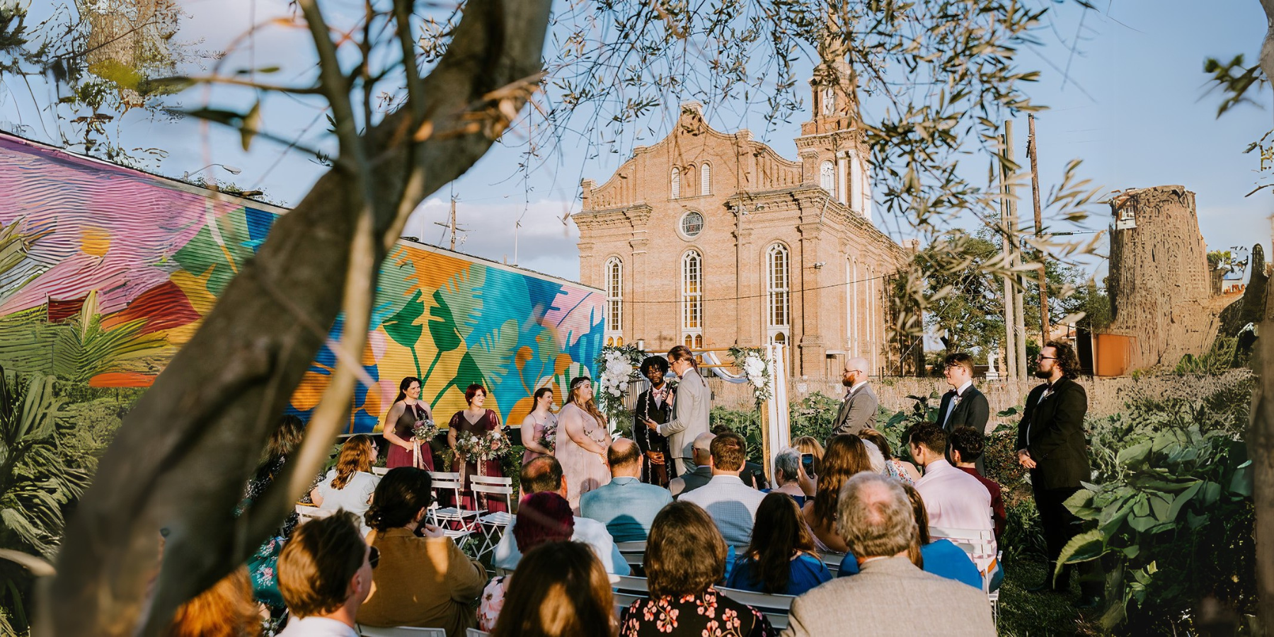 Outdoor wedding ceremony with a vibrant mural and historic church in the background