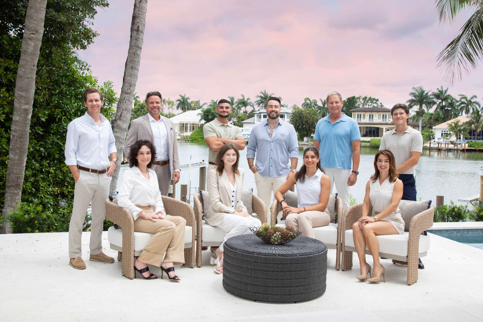 Group photo of eleven people outside by a waterfront, seated and standing in a relaxed pose