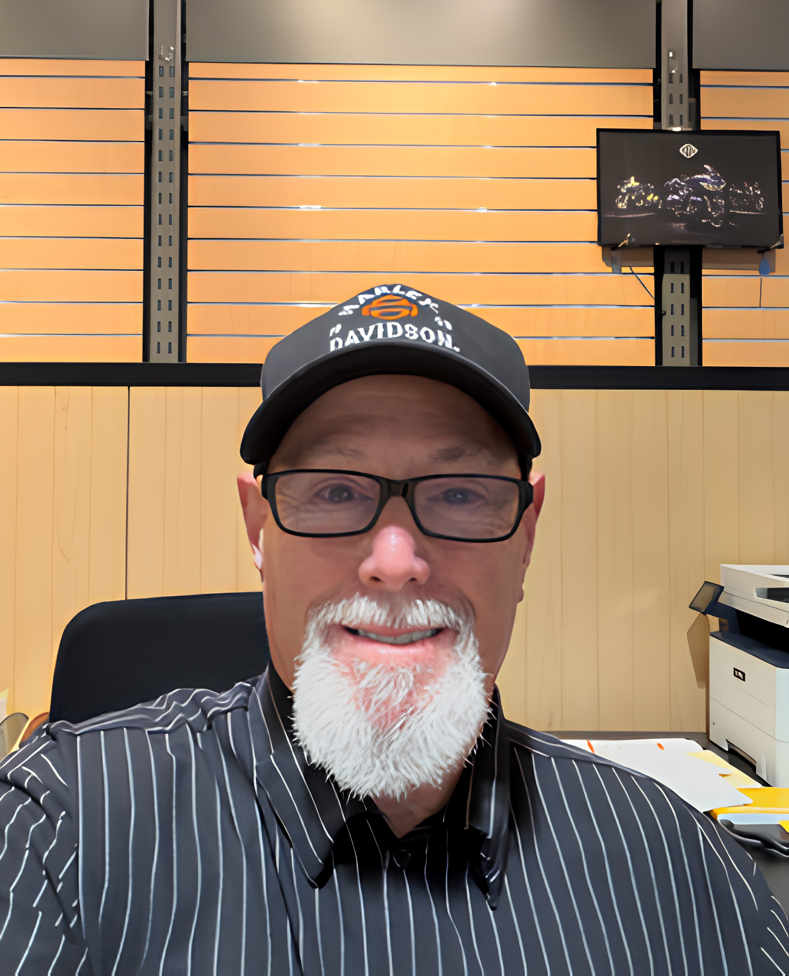 Man with glasses and a white beard wearing a cap, sitting at a desk