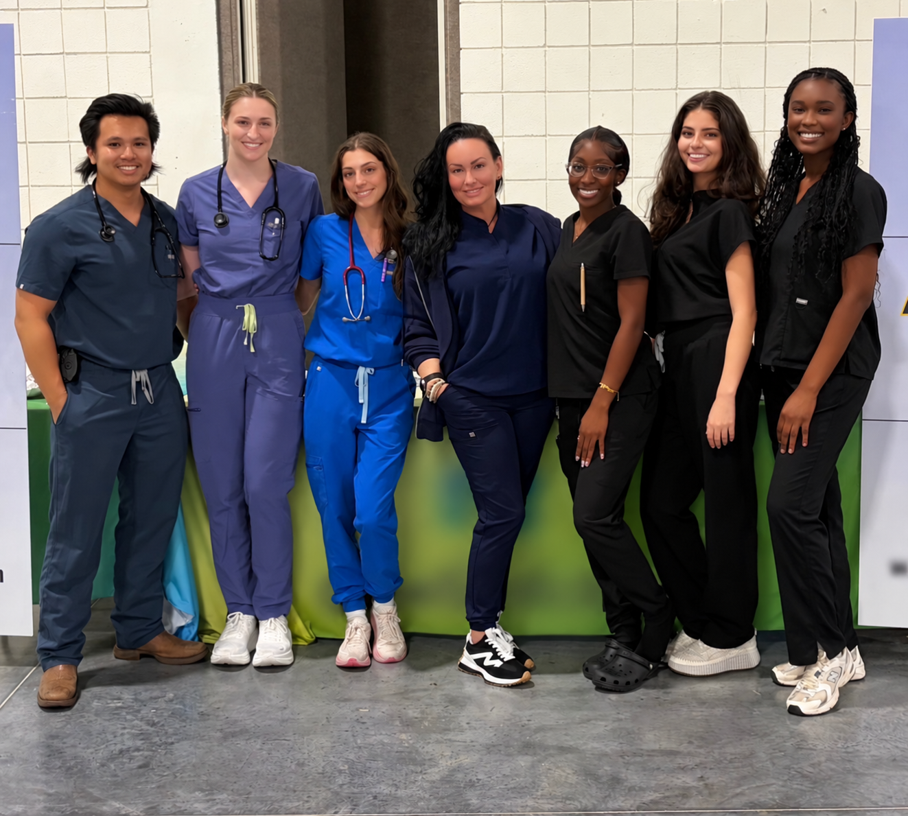 A diverse group of seven healthcare professionals in scrubs posing together at an event