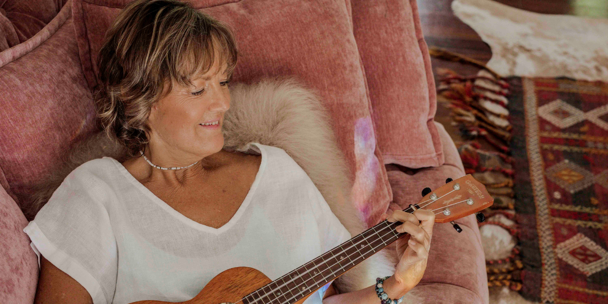 A woman playing a ukulele while seated on a pink sofa at home