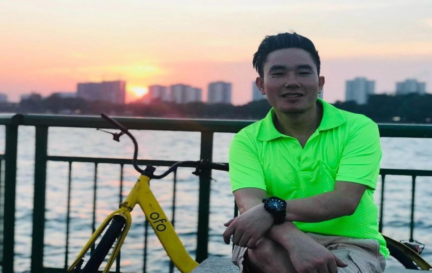 Person in neon green shirt sitting by a river at sunset with a bicycle