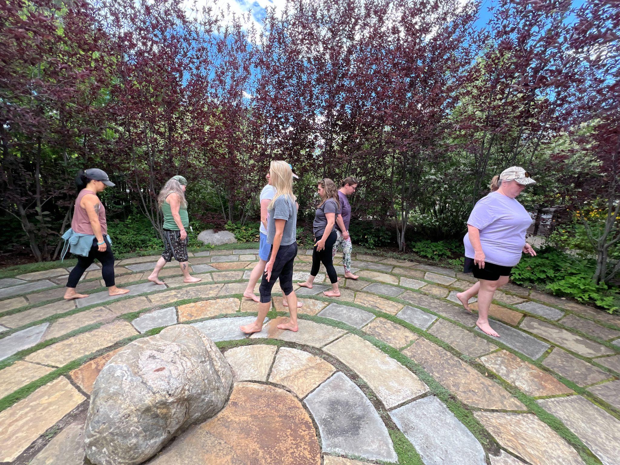 Group of people walking barefoot in a stone labyrinth surrounded by trees and shrubs