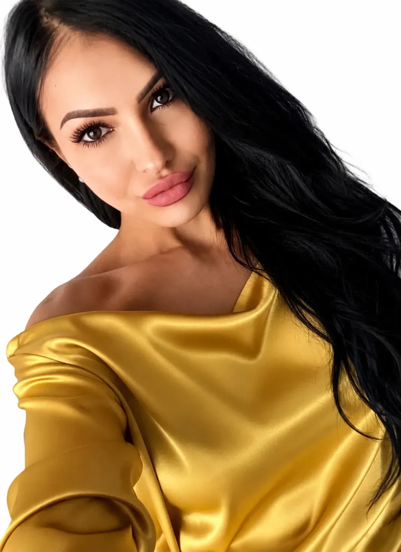 Woman with long black hair wearing a vibrant yellow satin top, posing for a selfie