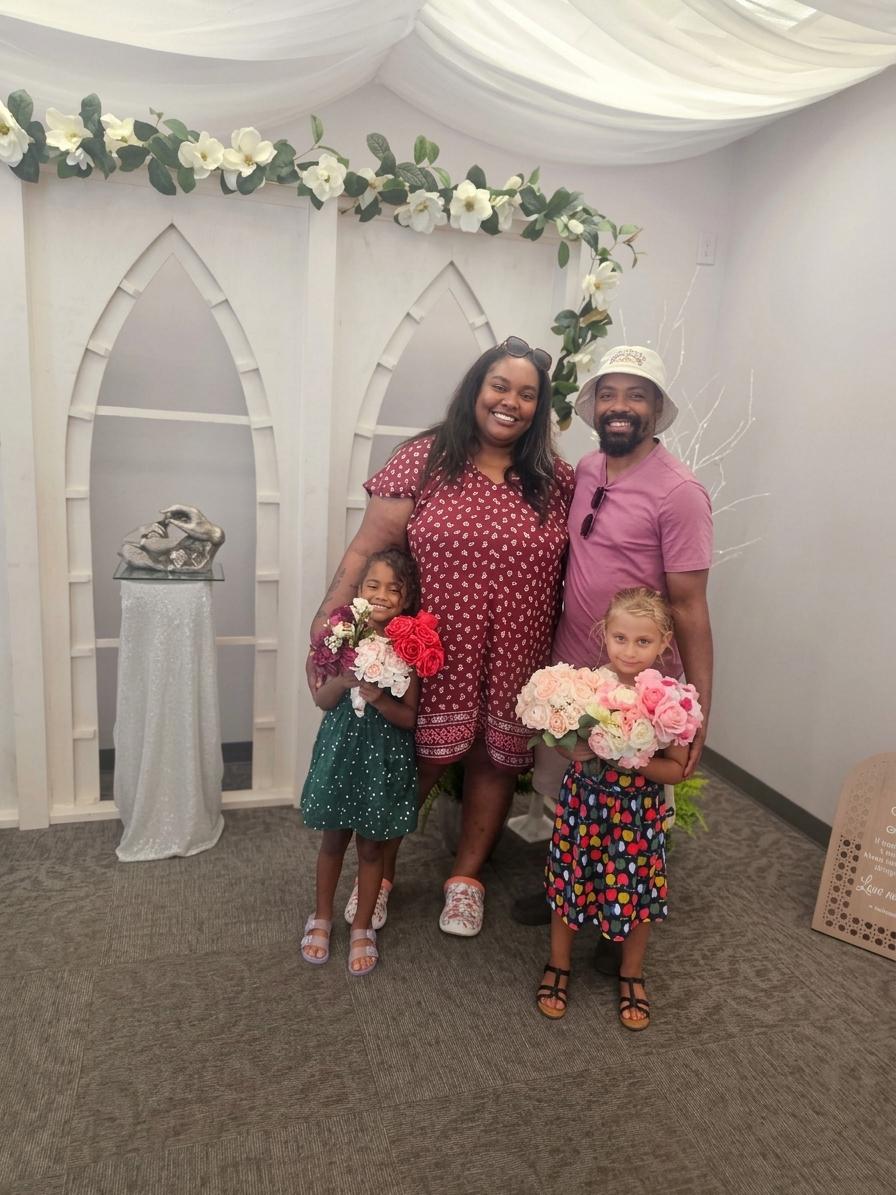 A family of four poses together holding flowers in a decorated indoor setting