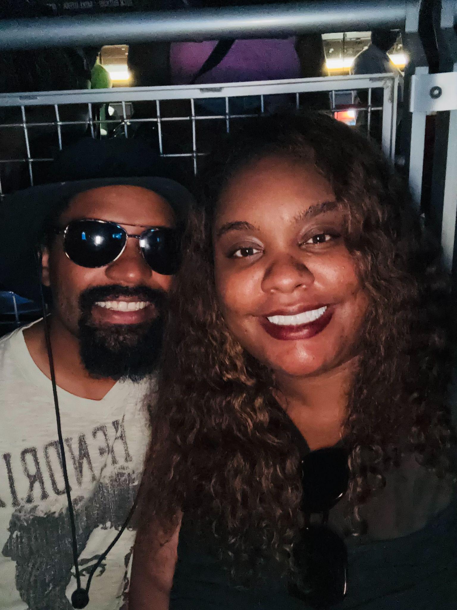 A man and a woman smiling together at an event, both wearing sunglasses