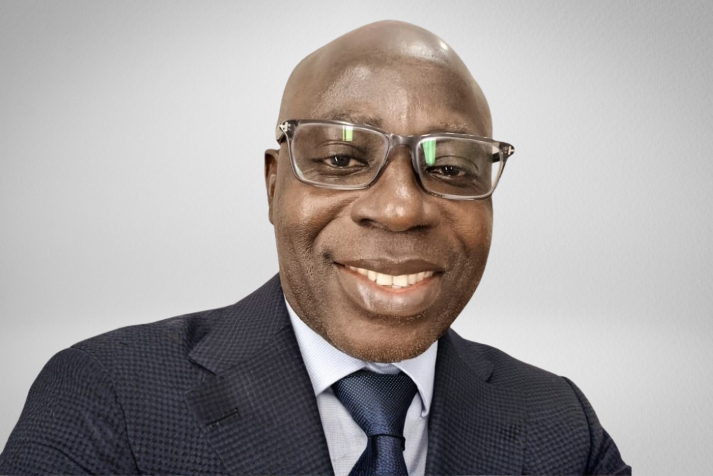 Smiling man in glasses wearing a suit and tie against a neutral background