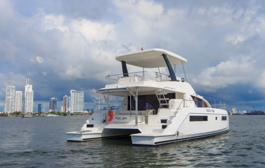 White catamaran yacht anchored in calm waters with a city skyline in the background