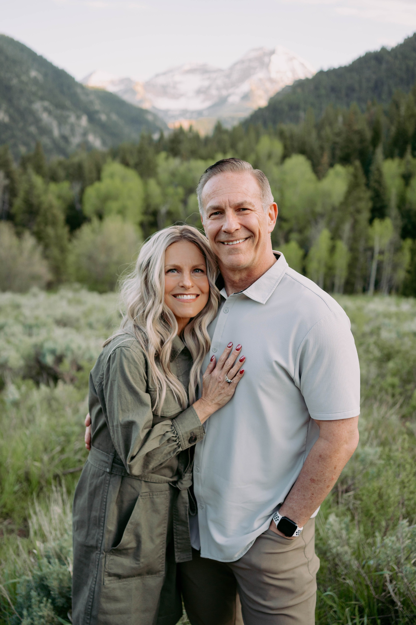A couple smiles joyfully together in a lush green landscape with mountains in the background