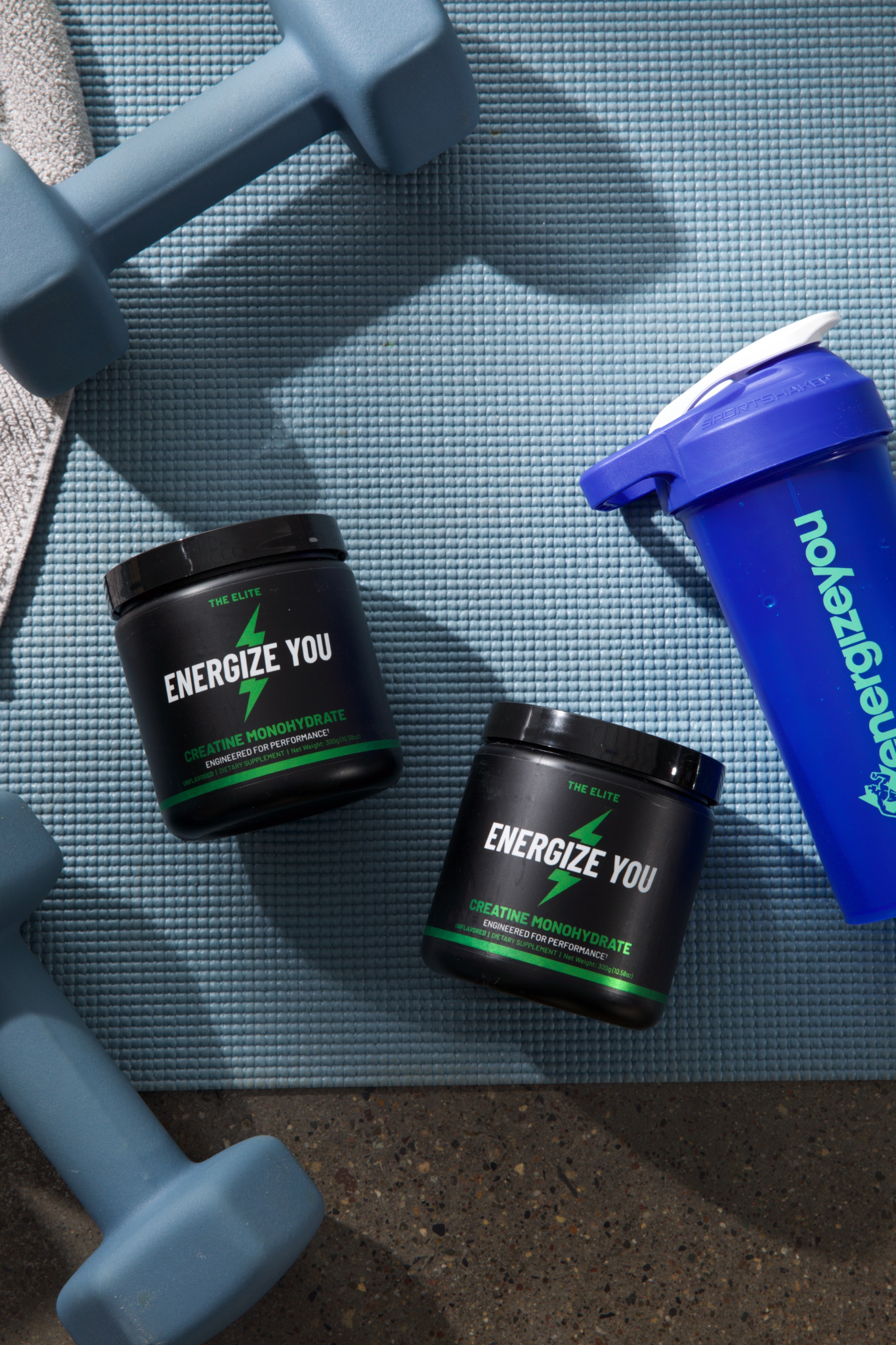 Dumbbells, supplement containers, and a shaker on a textured exercise mat