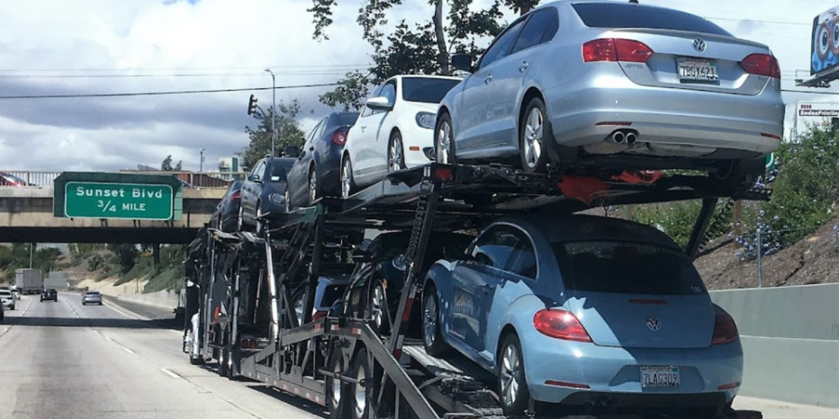 Car transport truck carrying multiple silver vehicles on a highway with overpass ahead