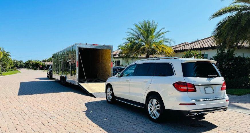 White SUV parked beside a large trailer on a sunny residential street