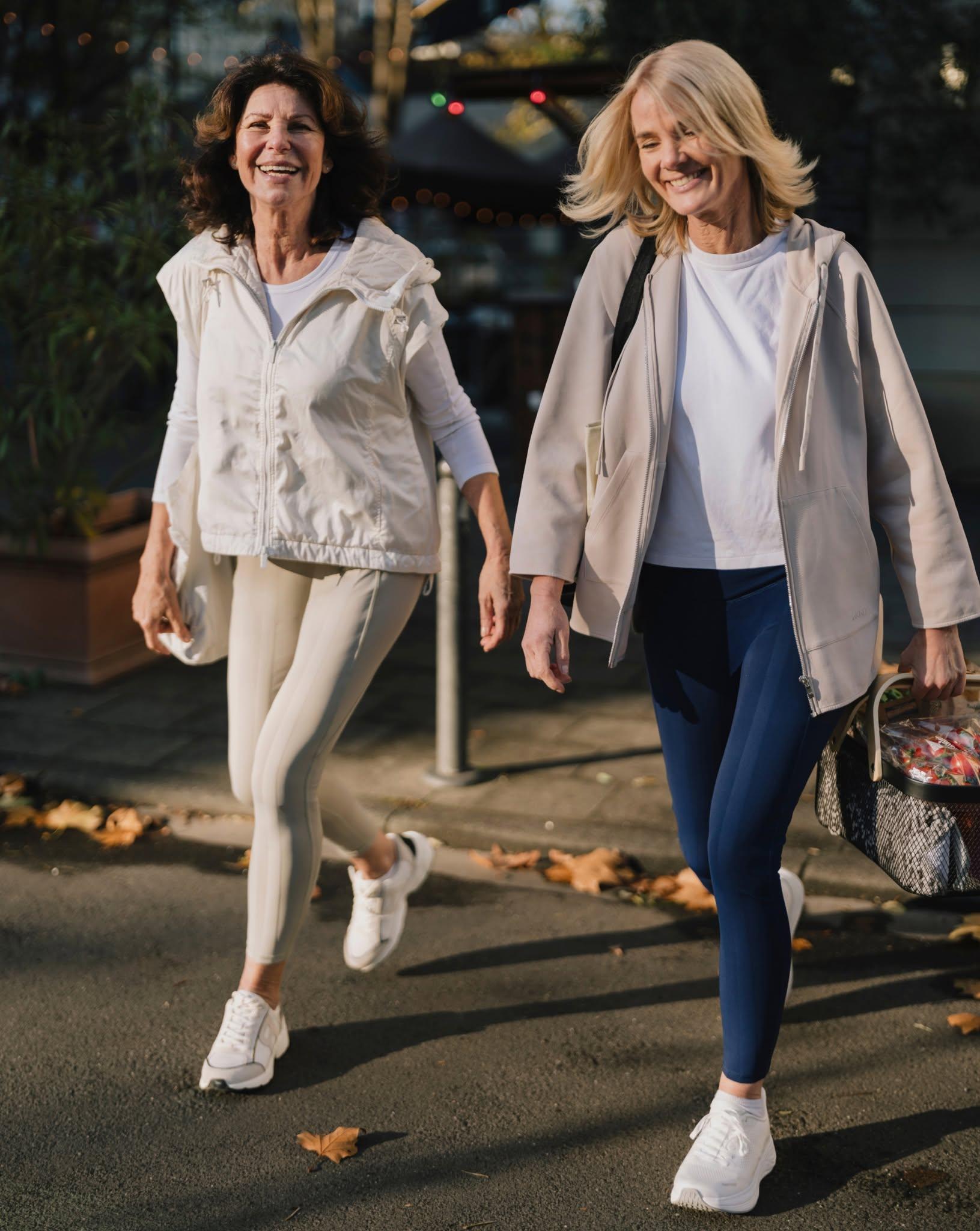 Two women in athletic wear walking together outdoors, smiling and enjoying a sunny day
