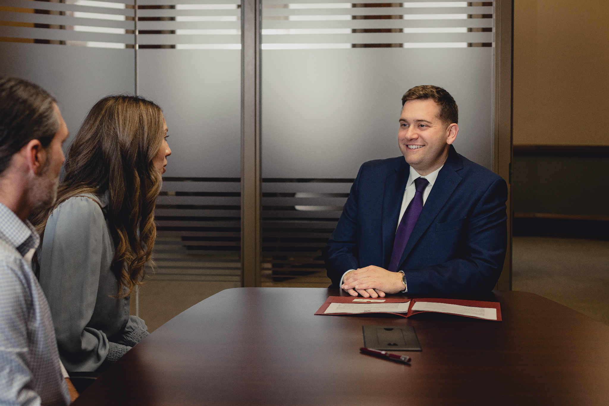 A man in a suit smiles at two people during a meeting at a table