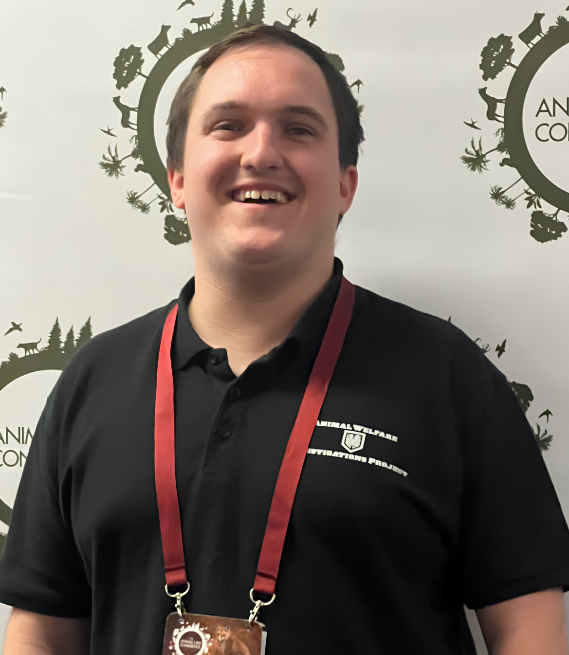Smiling young man wearing a black shirt and lanyard at an event backdrop