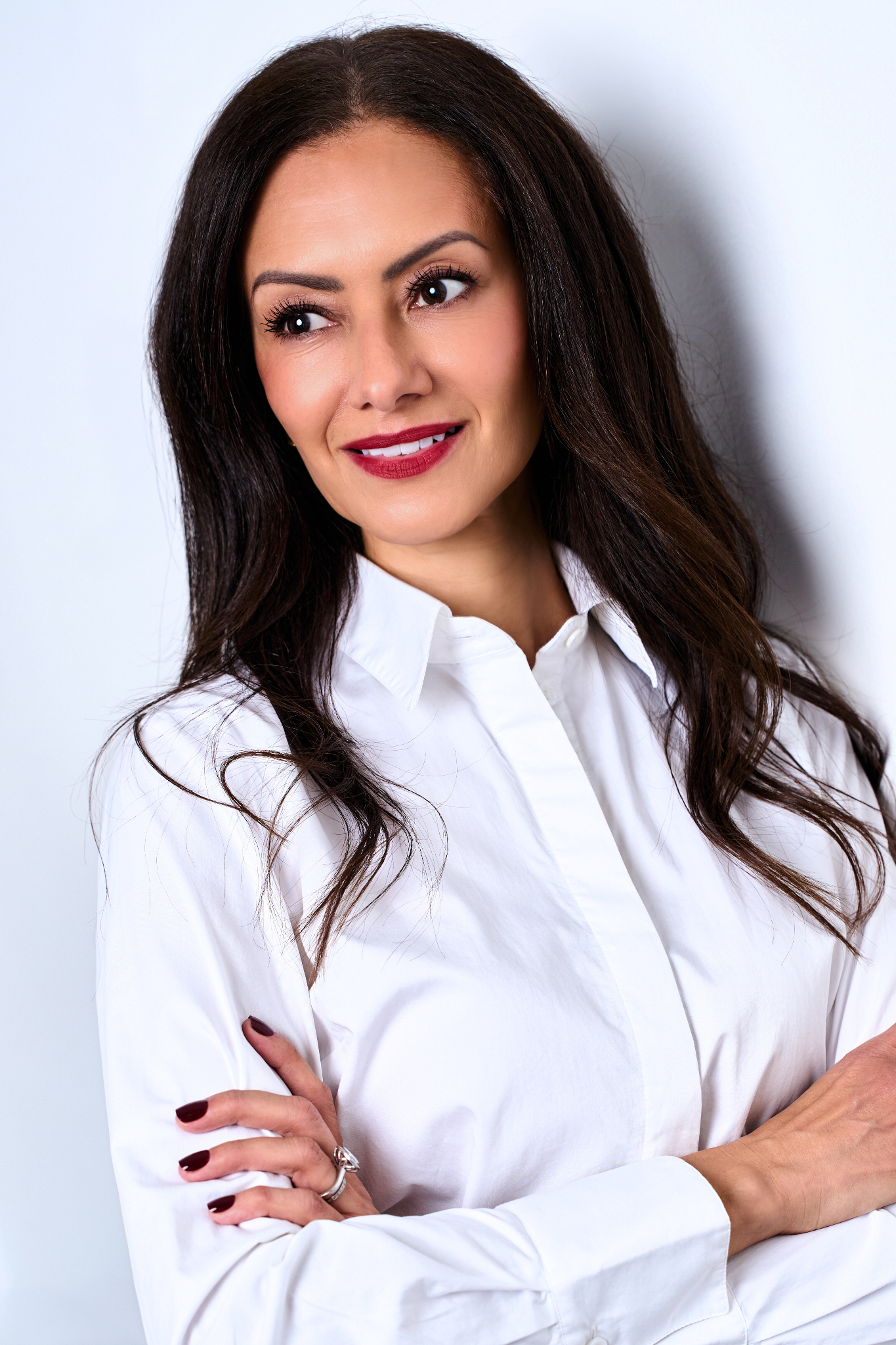 A woman in a white shirt poses confidently with a slight smile and long hair