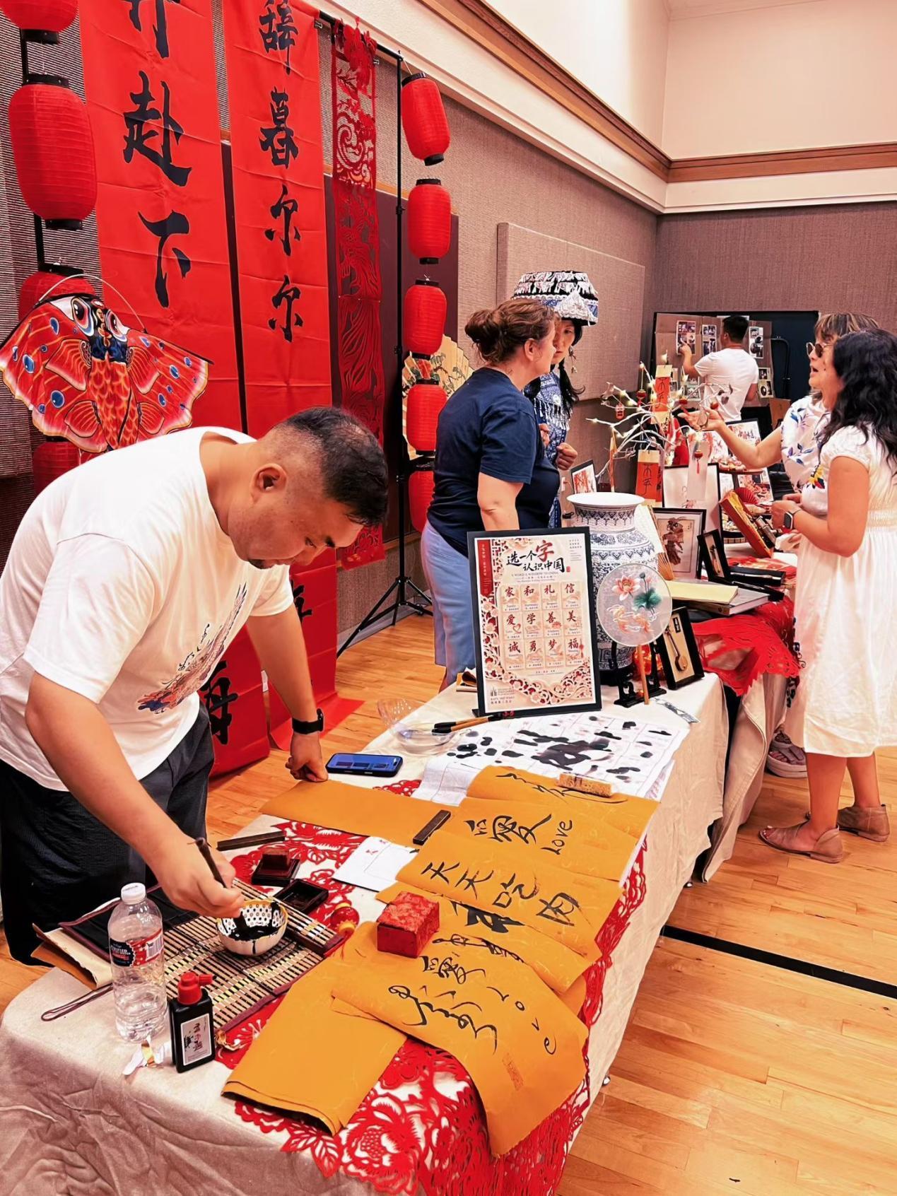 People at a cultural event display art and crafts on tables in a gymnasium
