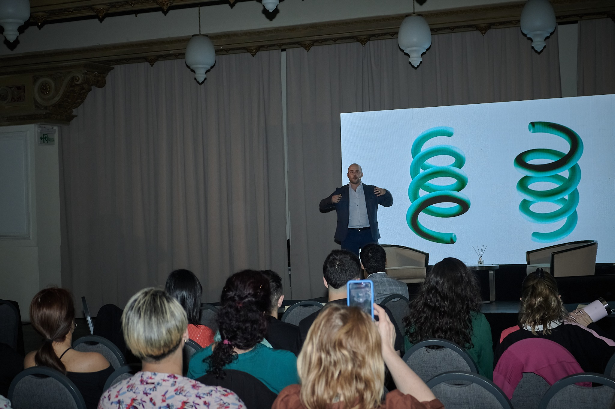 Speaker presenting on stage in front of an audience with a large screen behind