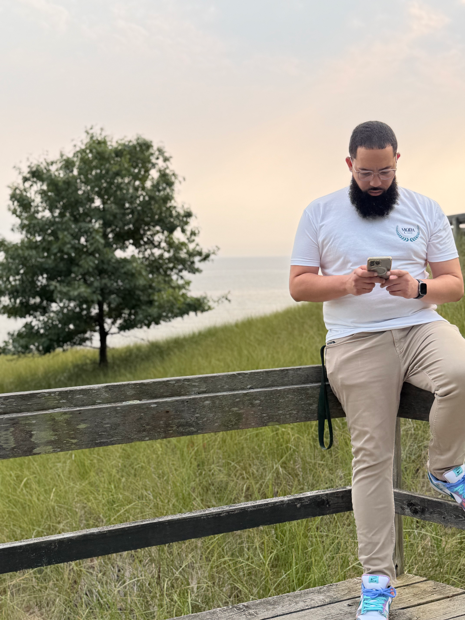 Person sitting on a wooden fence, using a phone with a scenic background