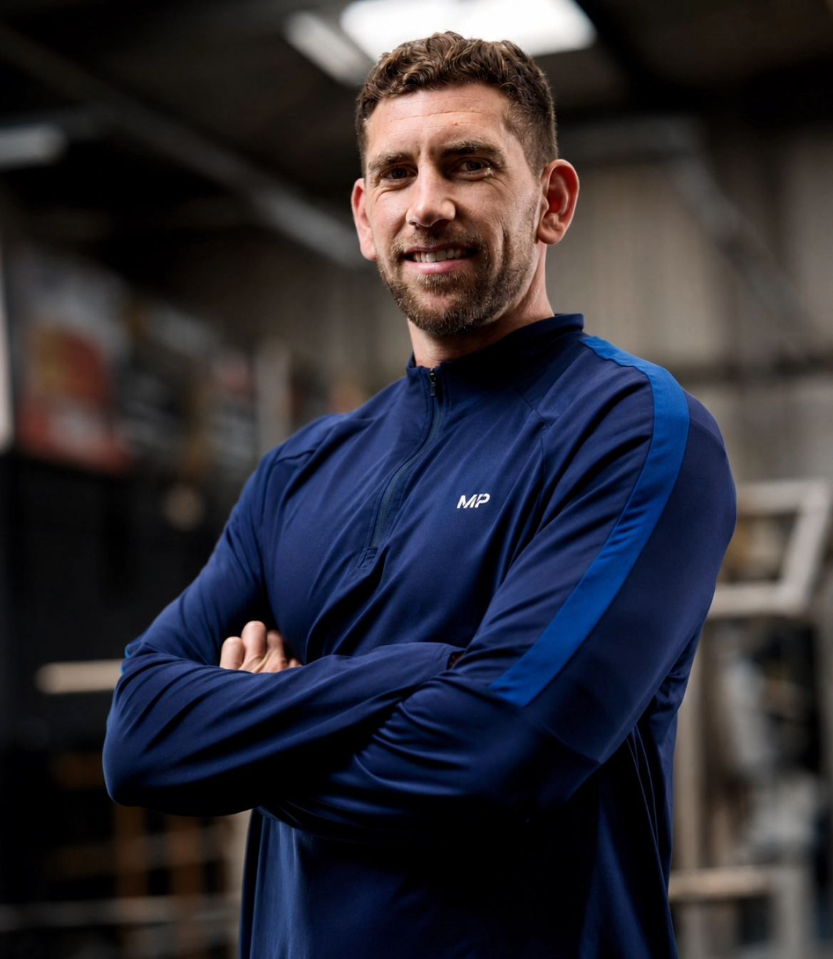 Man in a blue athletic jacket stands confidently with arms crossed in a gym