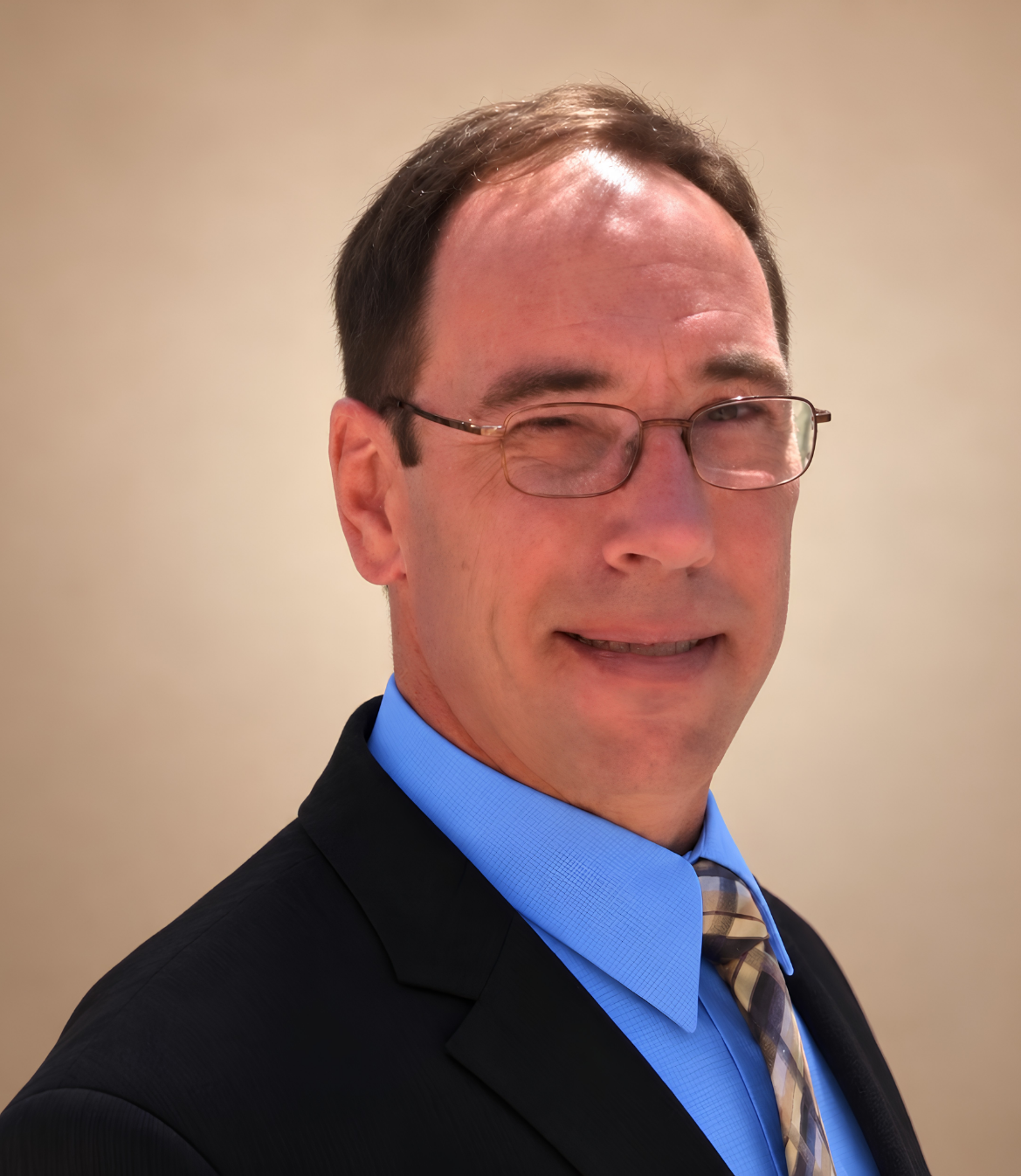 A man in business attire with glasses smiles against a neutral background