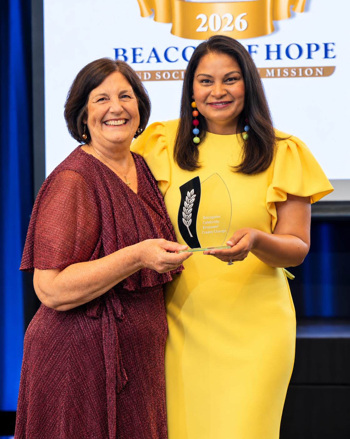 Two women smiling and posing with an award at a recognition event
