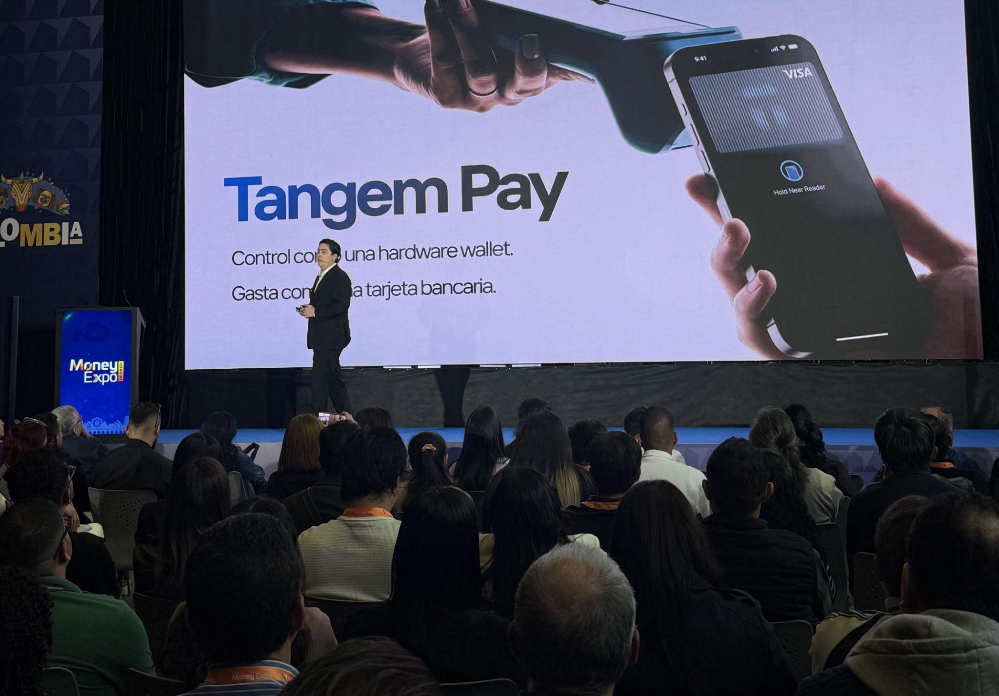 Presentation on Tangem Pay at a conference, featuring a speaker and a smartphone display
