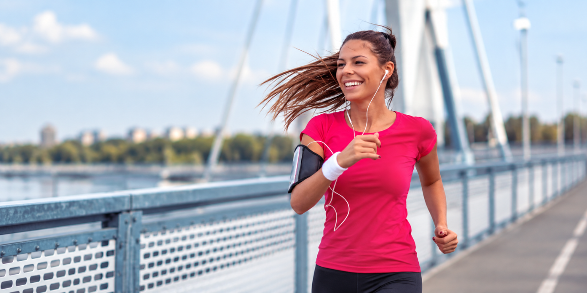 A woman jogs on a bridge, wearing headphones and a pink shirt.