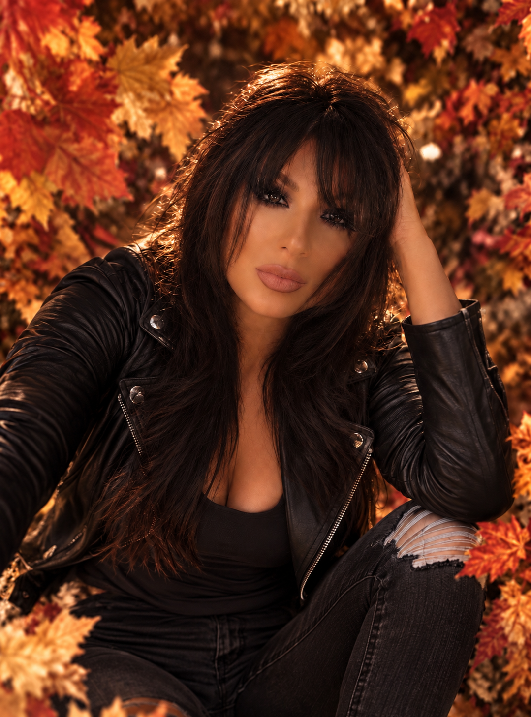 Woman in a black leather jacket poses among vibrant autumn leaves