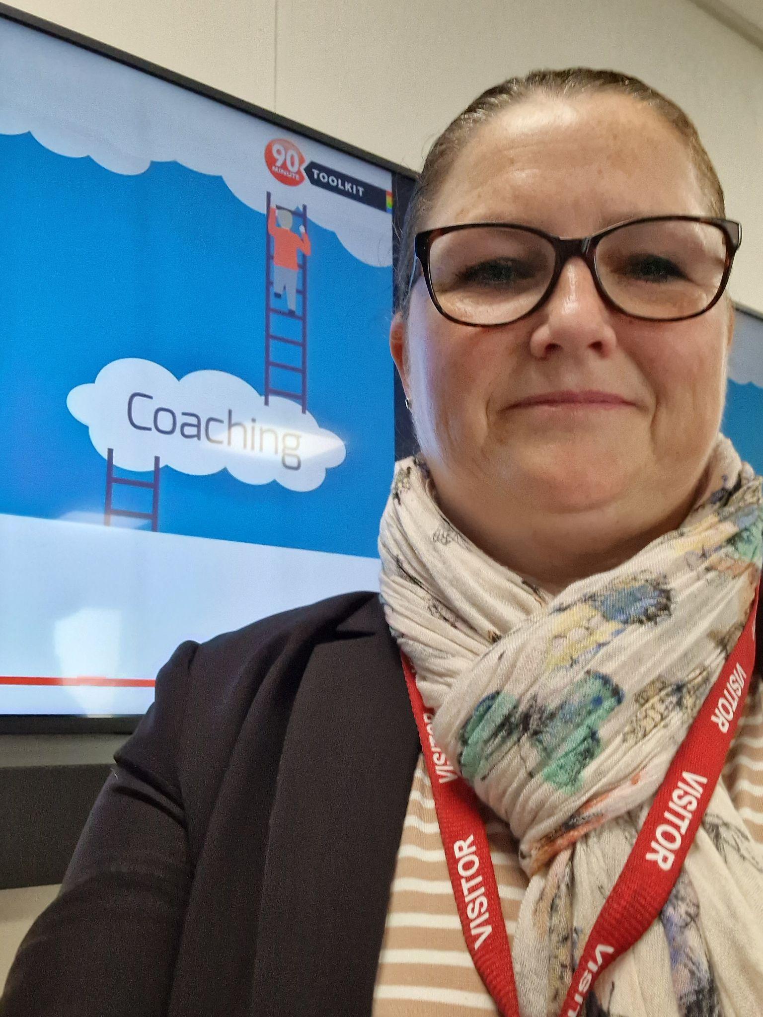 Person with glasses standing in front of a screen displaying "Coaching" and a ladder