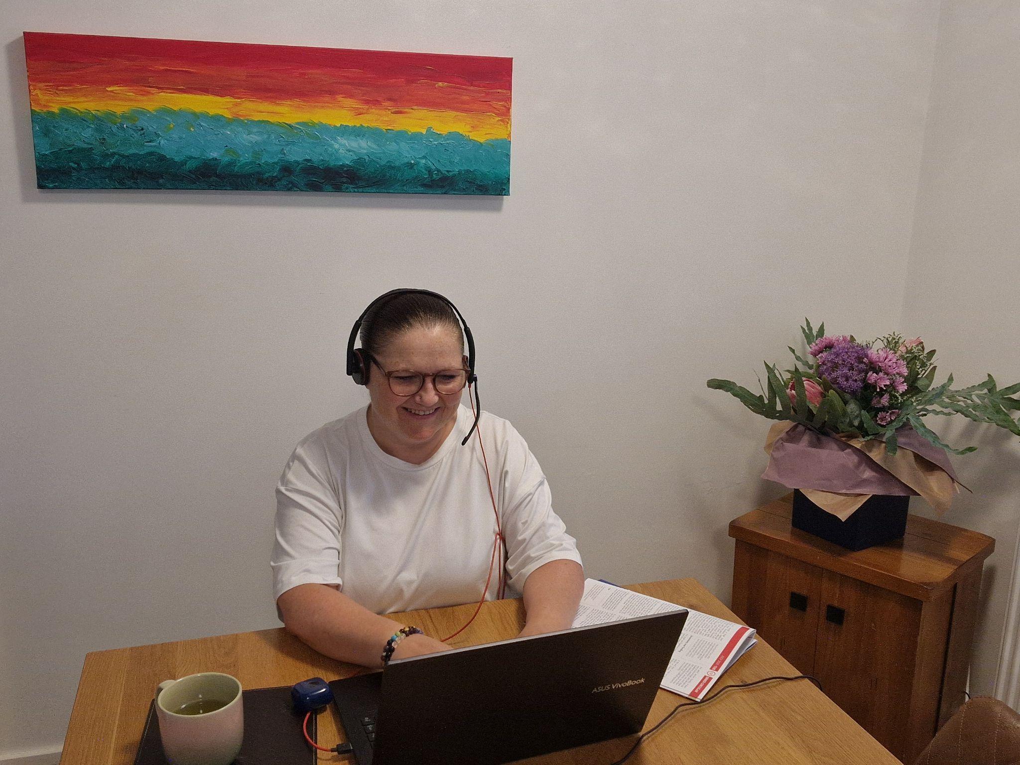 Person wearing headphones smiles while working on a laptop at a wooden table