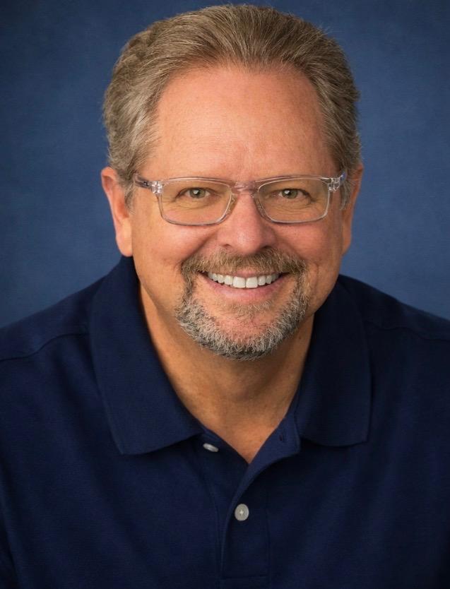 Smiling man with glasses and short gray hair wearing a navy blue shirt.