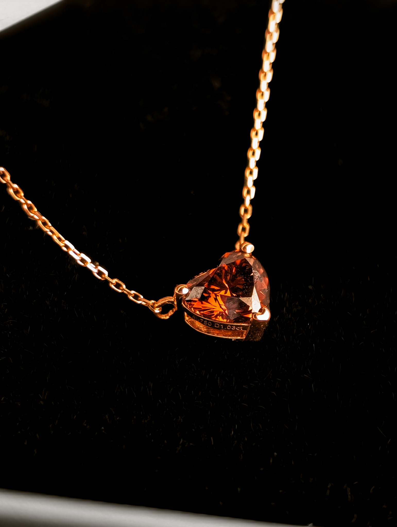 Close-up of a heart-shaped orange gemstone pendant on a delicate gold chain