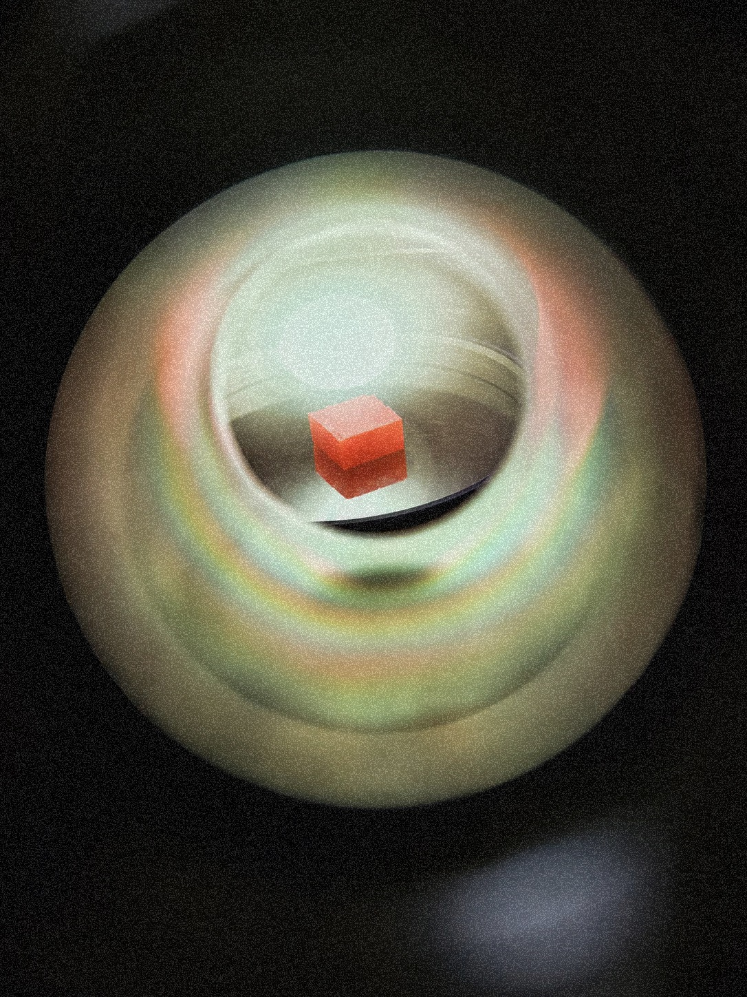 A small red cube sits inside a circular, reflective surface with colorful gradients.