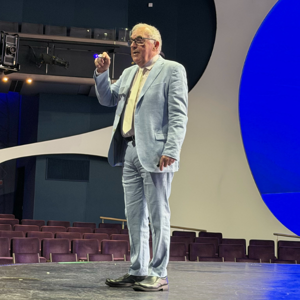 Man in a light blue suit presenting on stage with a blue backdrop