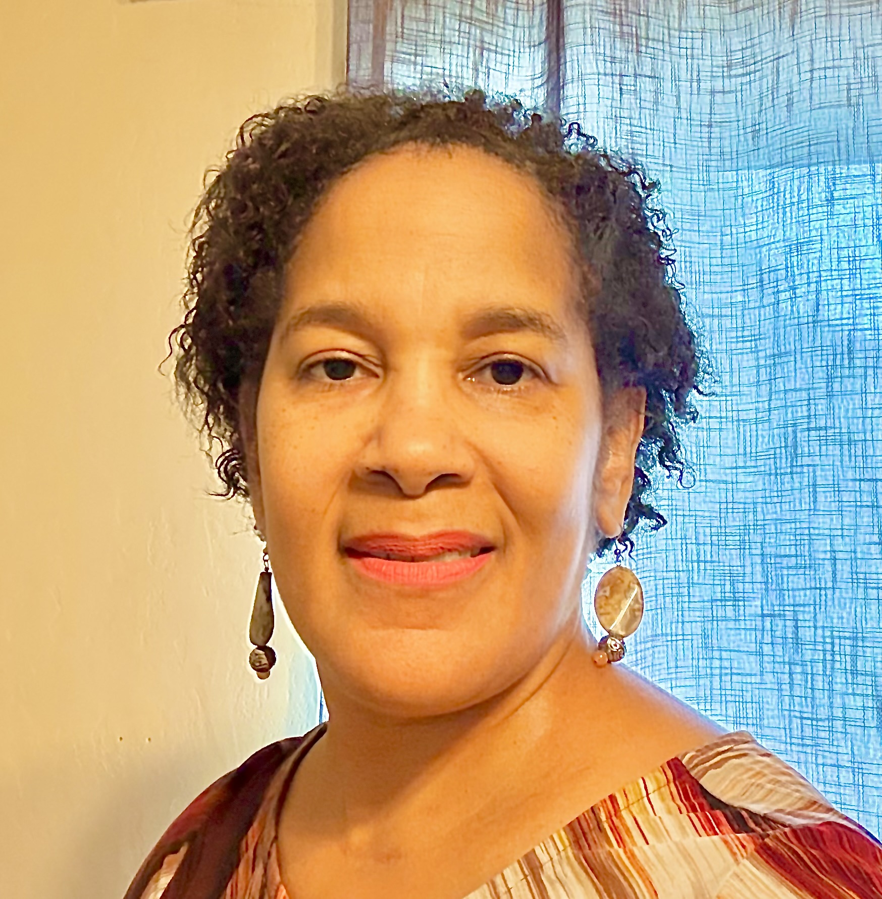 A woman with curly hair wearing earrings and a colorful striped top