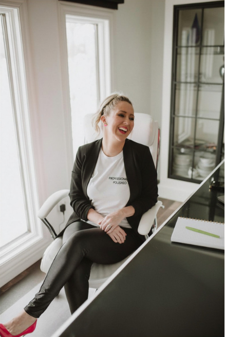 A smiling woman in a blazer and shirt sits in a modern office chair.