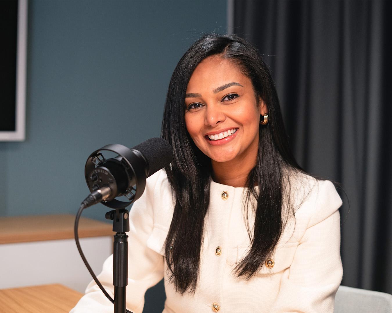 Woman smiling in a podcast studio with microphone and modern decor behind her