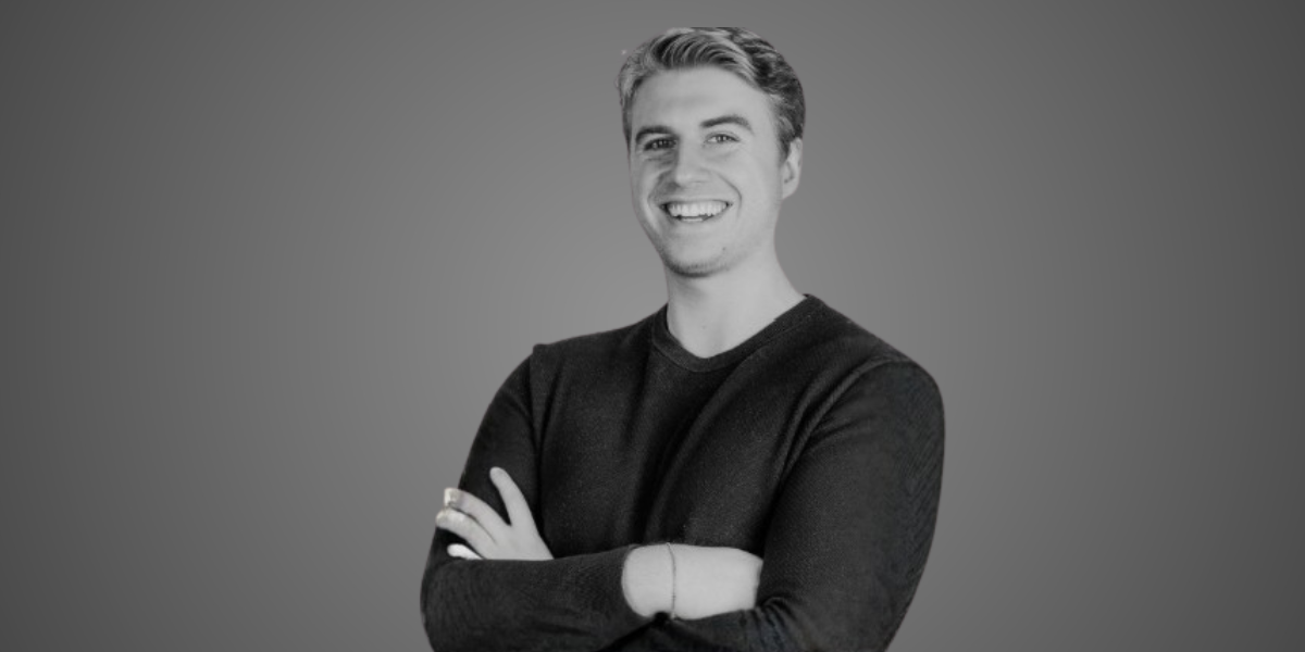 Smiling young man with crossed arms wearing a black sweater against a gray background
