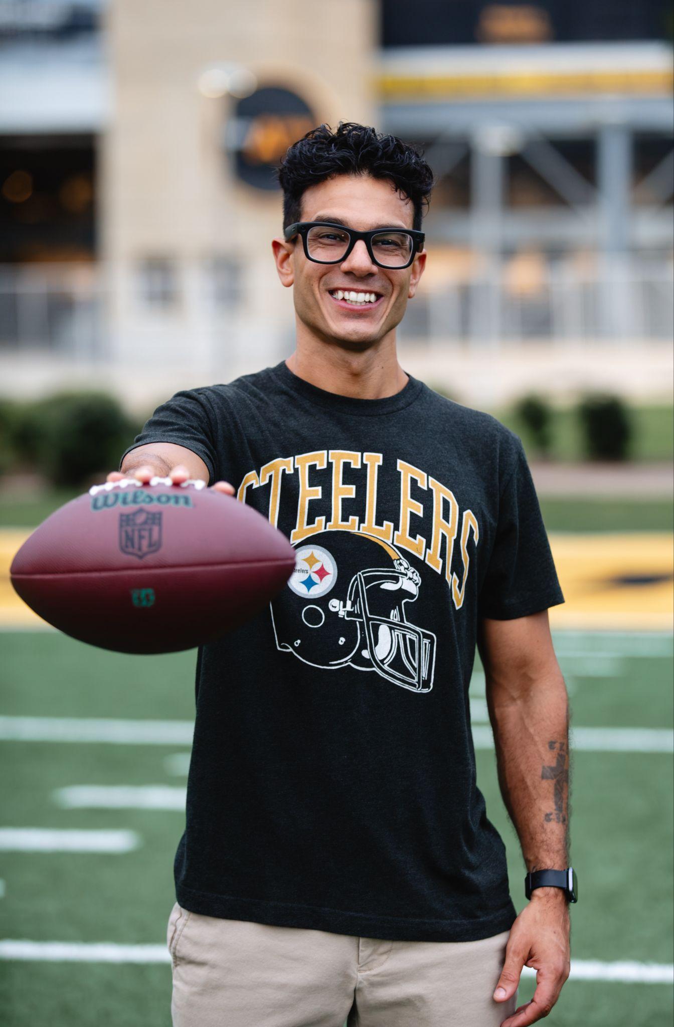 Smiling man in a Steelers shirt holding a football on a field