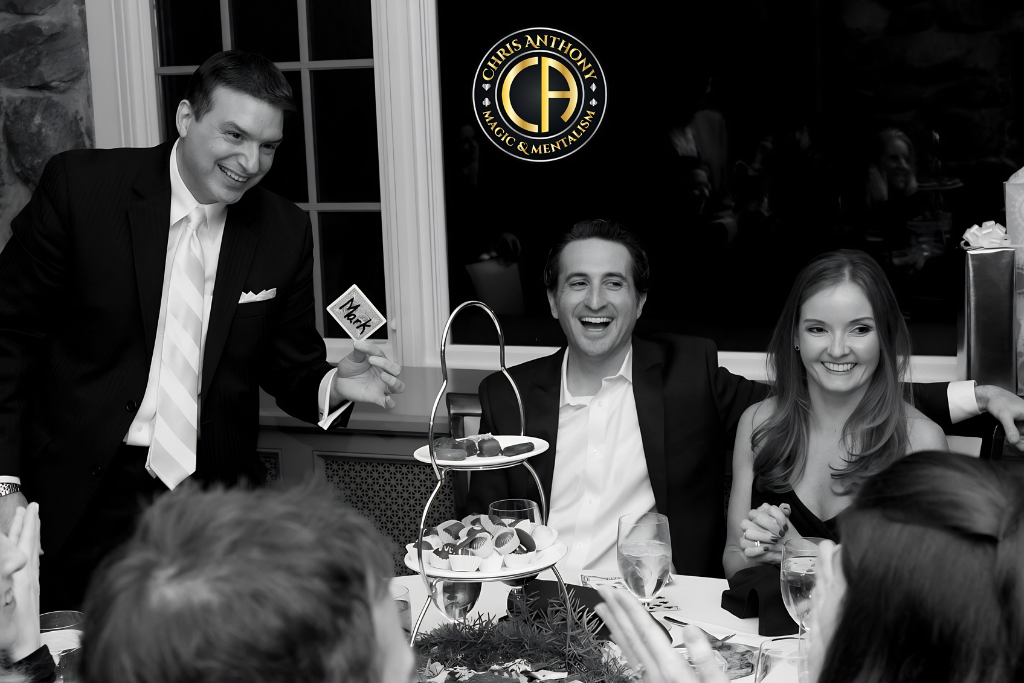 A magician performs at a dinner event with guests enjoying dessert and laughter.