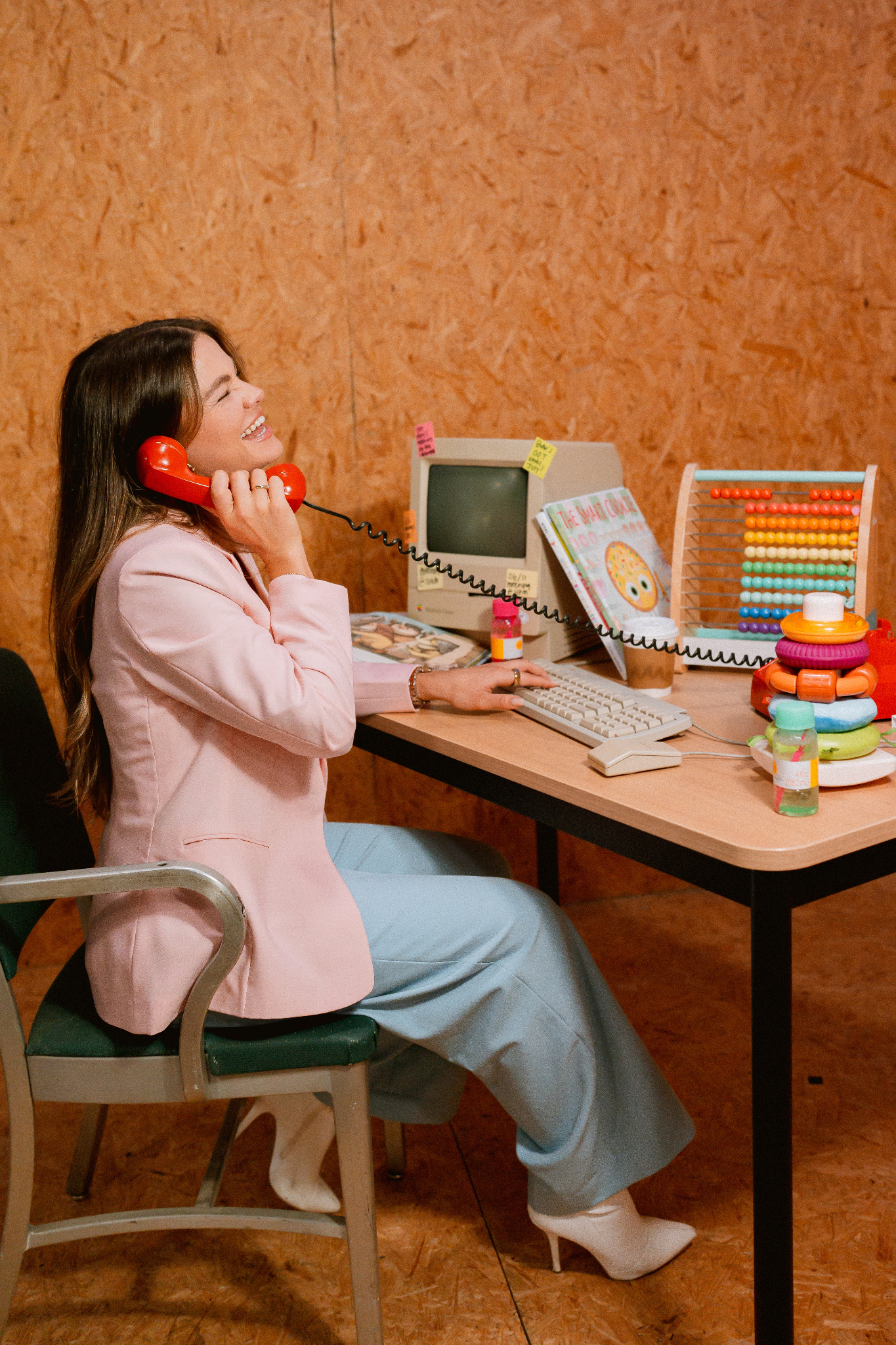Woman in a pink blazer sitting at a retro desk using a red phone