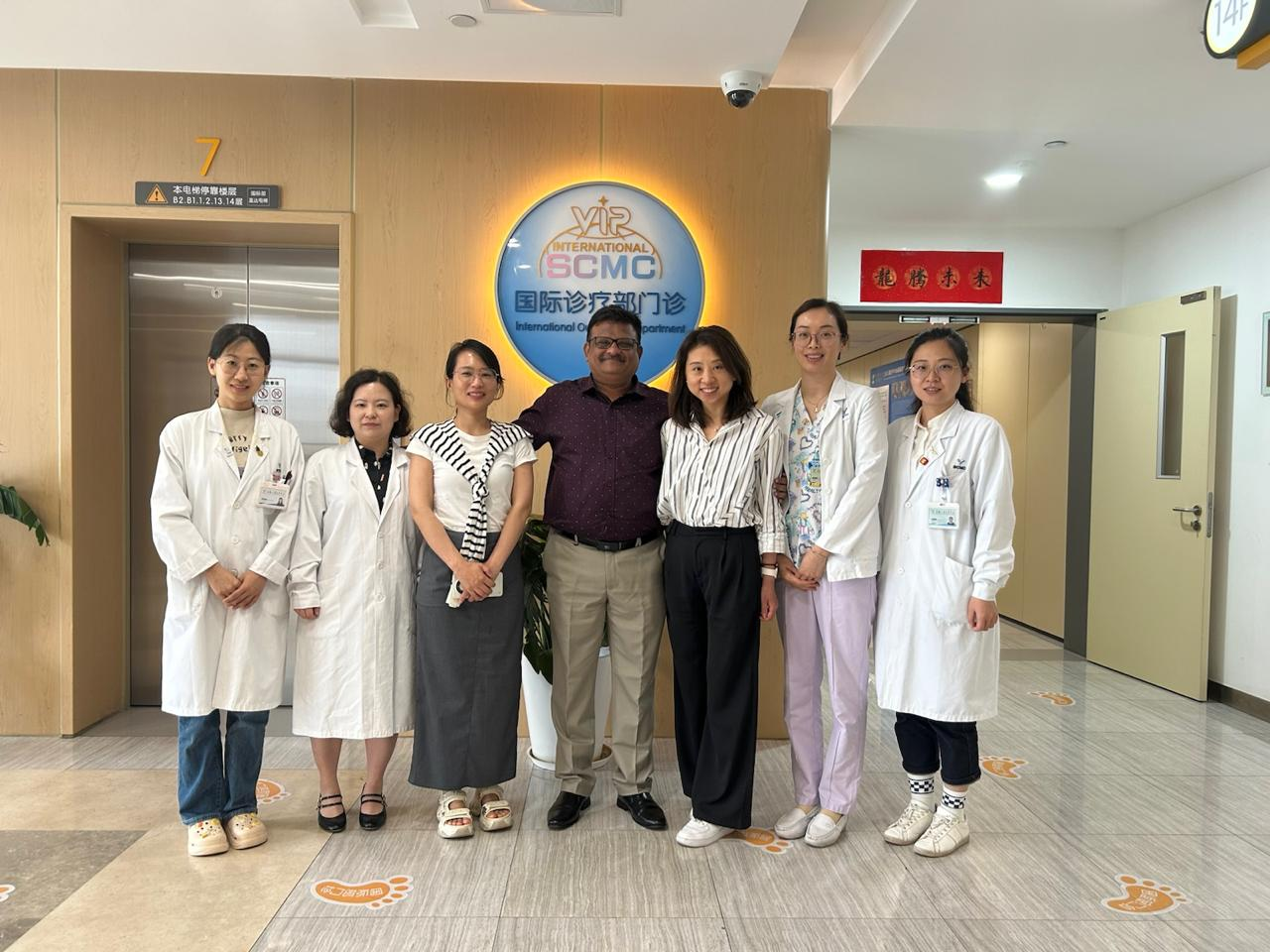 Group of seven medical professionals posing in a hospital lobby with a welcoming atmosphere