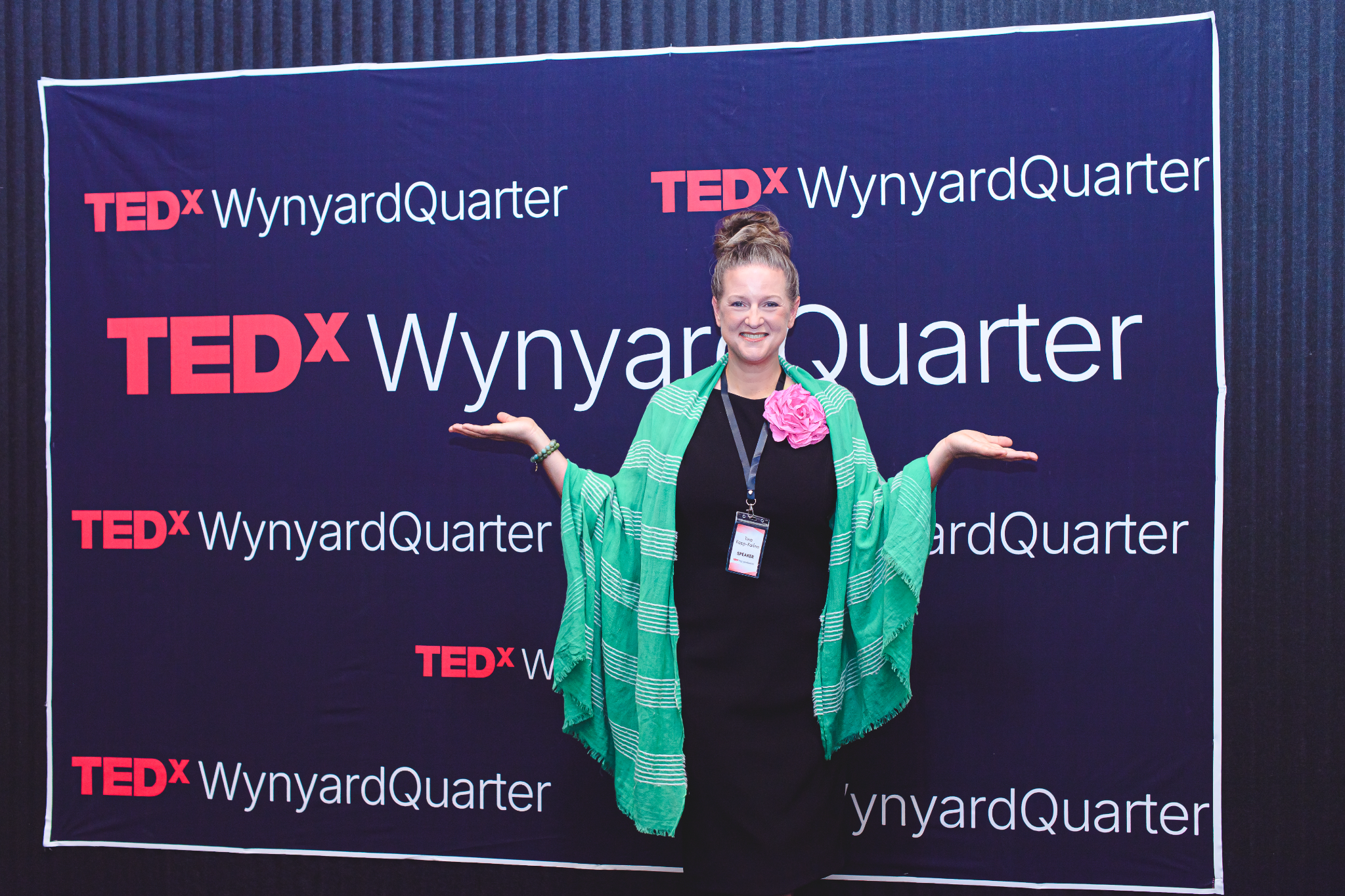 Woman in a green shawl poses in front of a TEDx WynyardQuarter backdrop