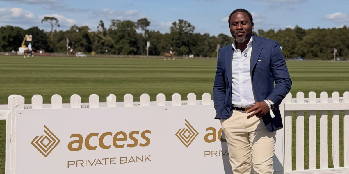 A man in a blazer stands beside an Access Private Bank sign on a polo field