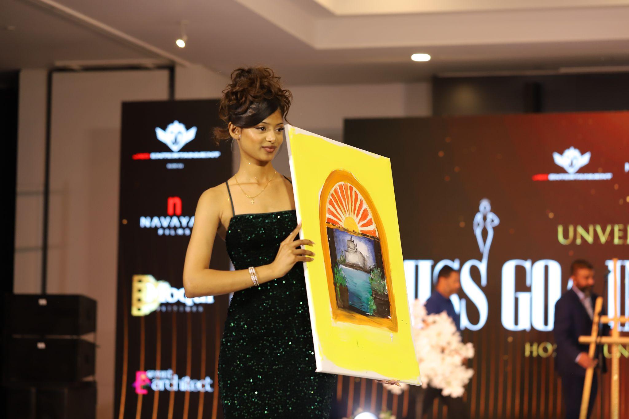Model in a green dress holding a colorful painting on stage